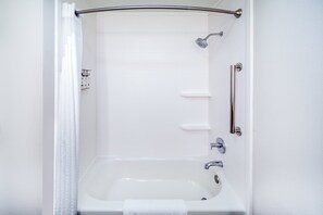 A modern bathroom with a bathtub, shower, and grab bars.