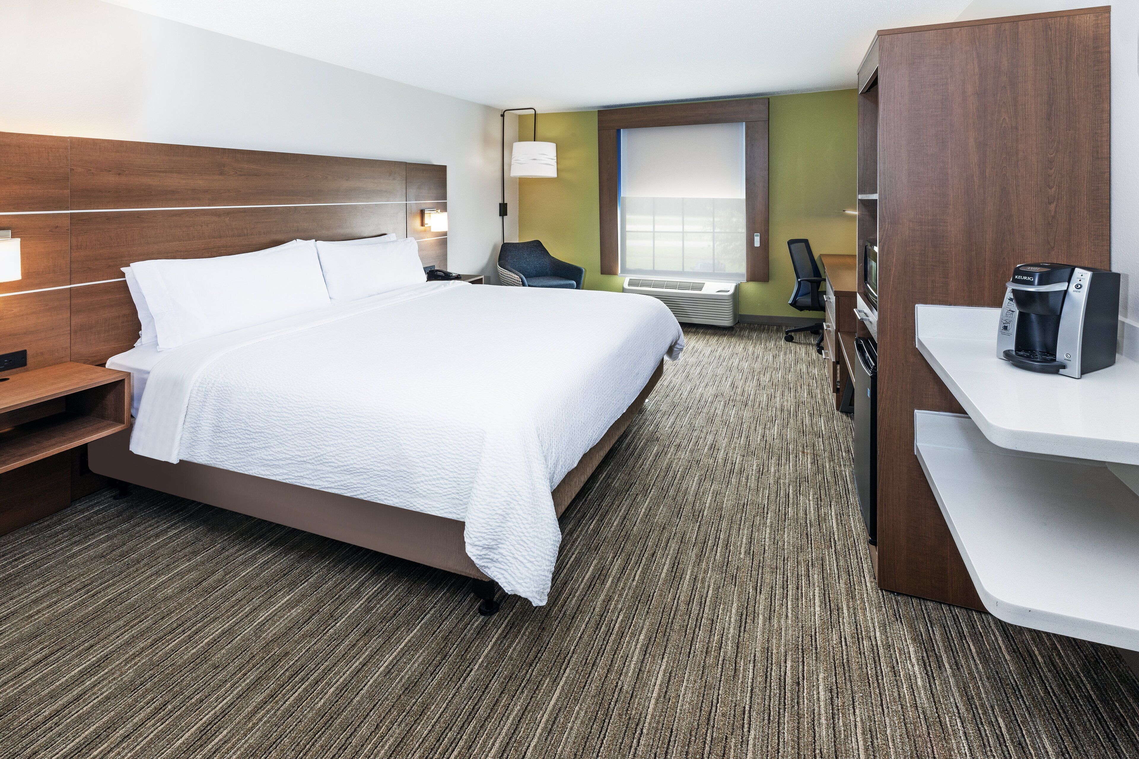 Une chambre d’hôtel avec un grand lit, un bureau, une chaise, un minibar et une fenêtre.