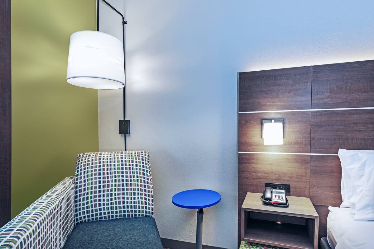 A hotel room with a bed, a small bedside table with a phone, a blue round table, a patterned sofa, and a hanging lamp.