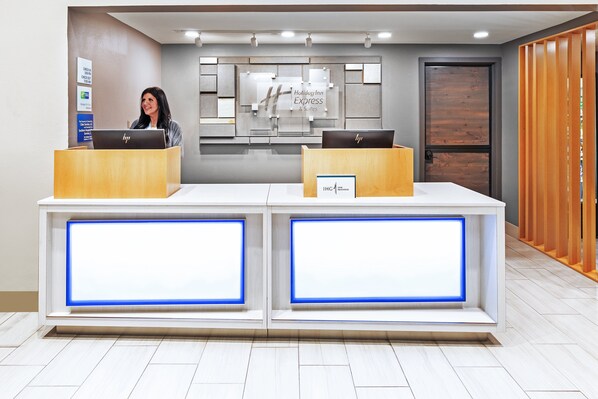 A hotel reception desk with two computer stations, a sign for Holiday Inn Express & Suites, and a wooden partition on the right. - Holiday Inn Express & Suites Sulphur (Lake Charles) by IHG (Sulphur)