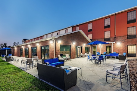 An outdoor patio area with seating and tables, a brick building, and a clear sky.
