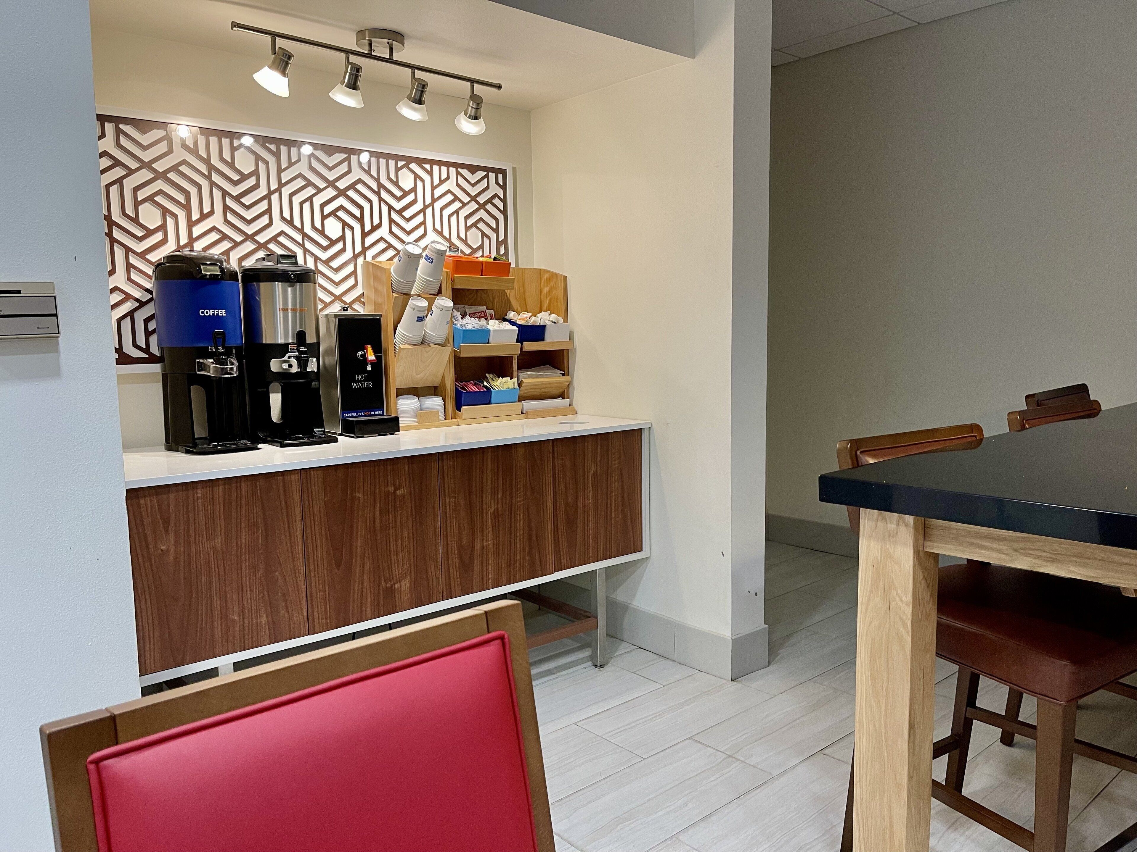 Une chambre d’hôtel moderne avec un comptoir en bois, des machines à café et un coin repas comprenant une table et des chaises.