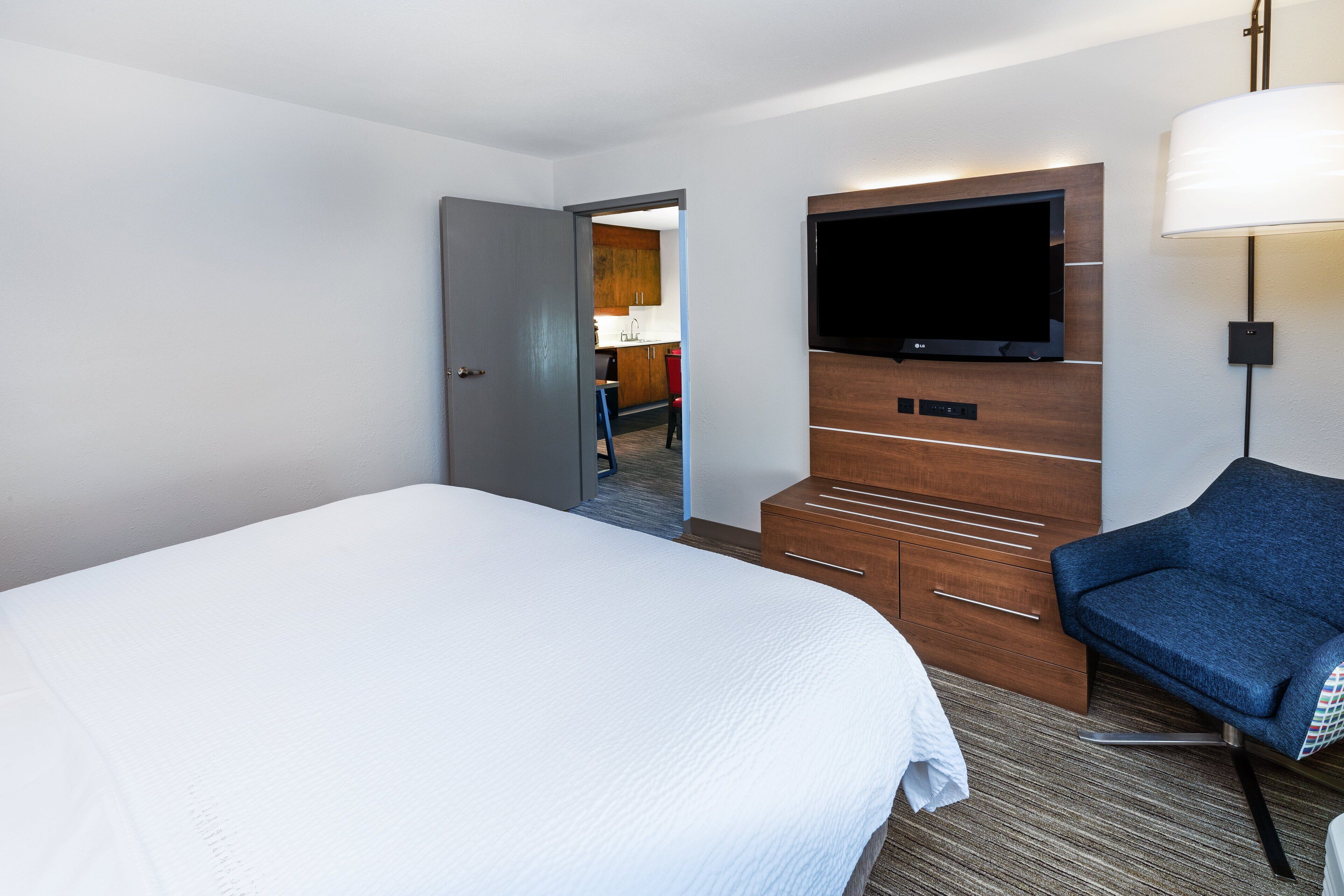 A hotel room with a large bed, a TV mounted on the wall, a desk, and a chair.