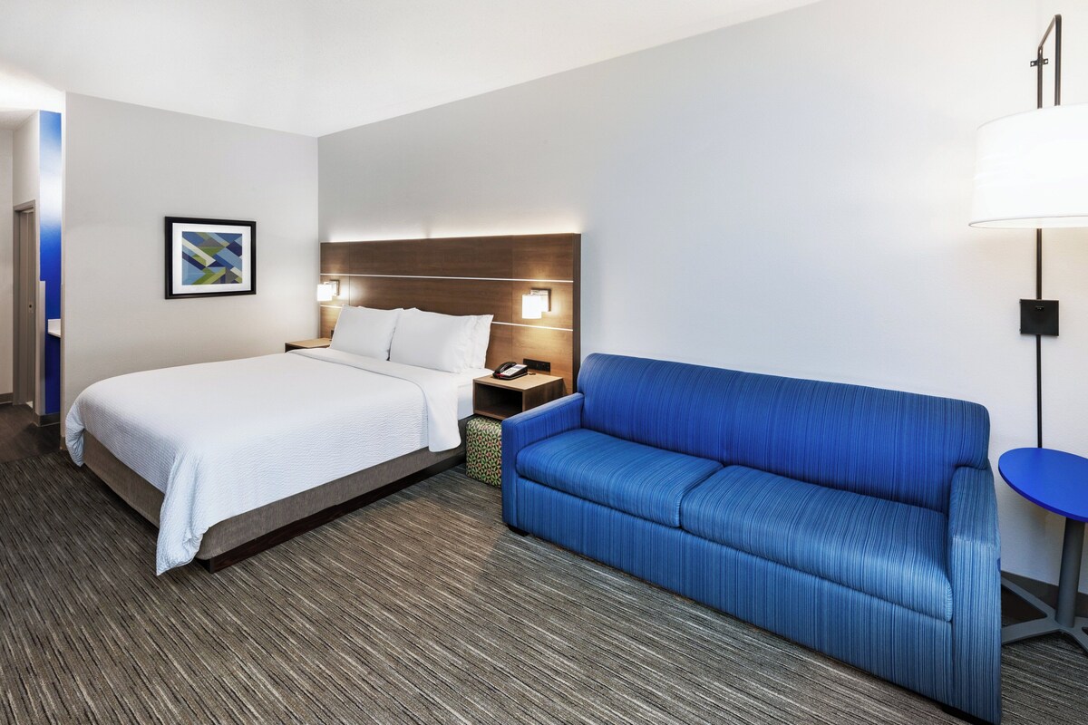 Una habitación de hotel con una cama, un sofá azul, una mesita de noche con una lámpara y un cuadro en la pared.