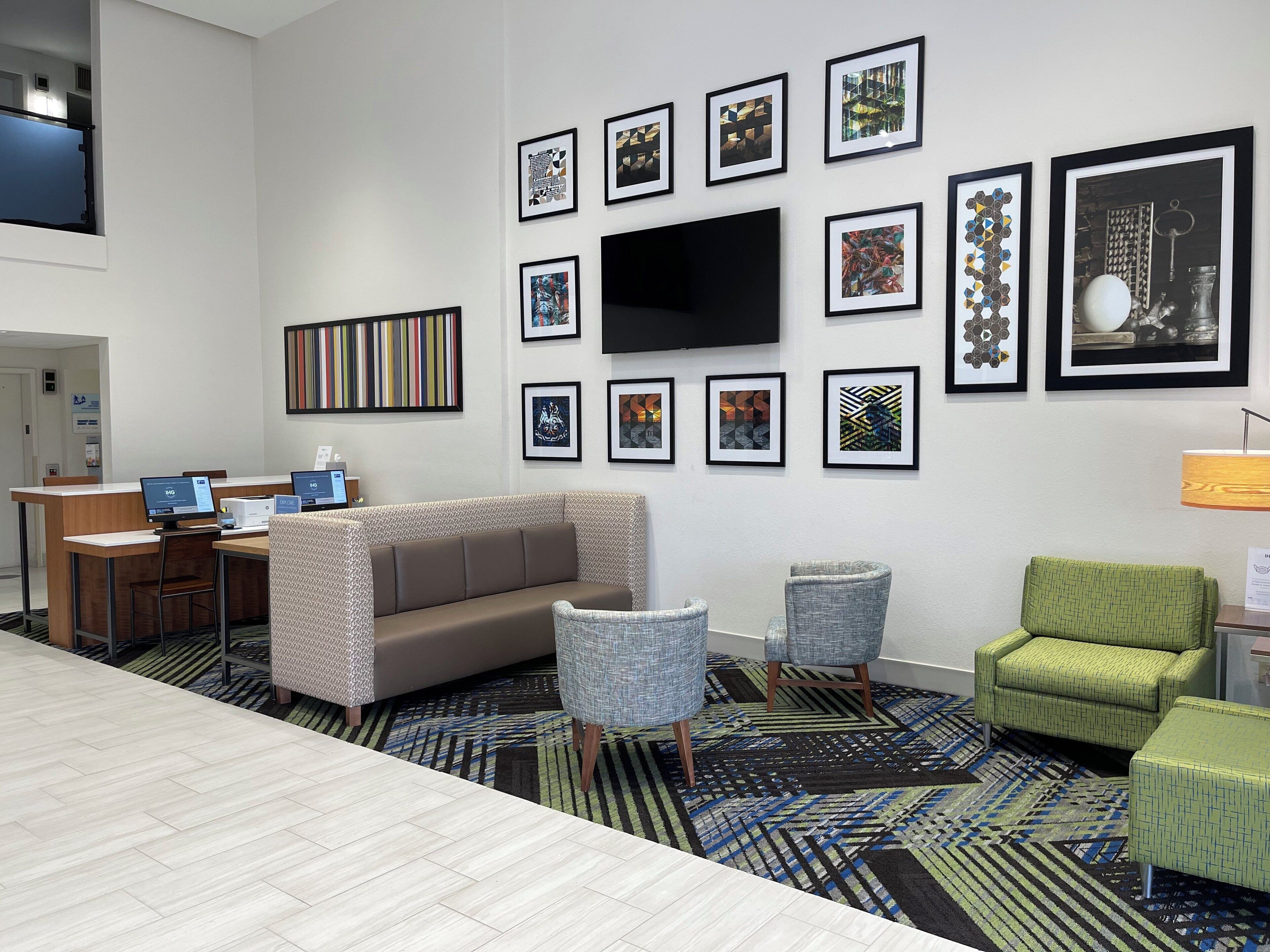 A hotel lobby with a sofa, chairs, a TV, and framed artwork on the wall.