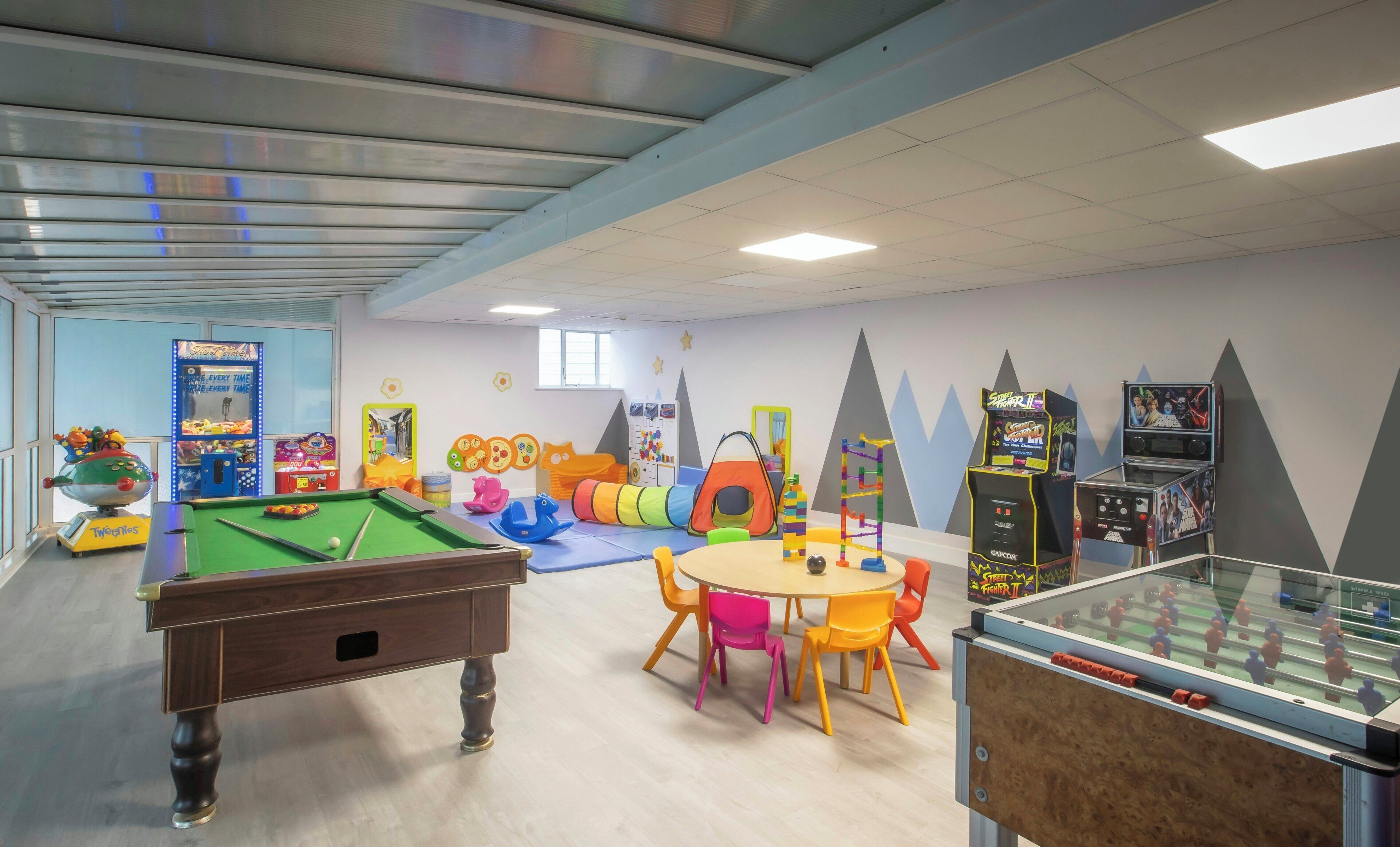 Ein Kinderspielbereich mit Billardtisch, Spielautomaten und verschiedenen Spielgeräten.