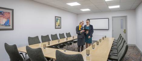 Une salle de conférence équipée d’une longue table, de chaises et d’un écran de projection.