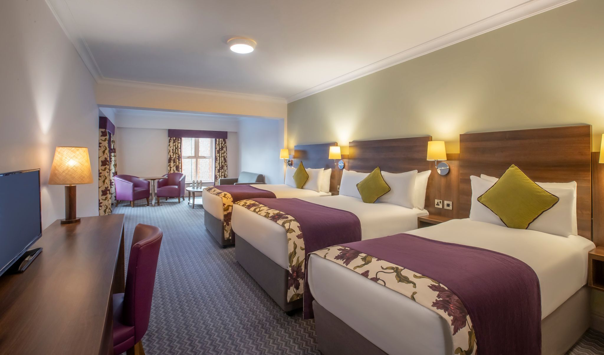 Une chambre d’hôtel avec deux lits, un bureau, une chaise et un téléviseur.