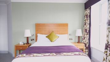 A hotel room with a large bed, two bedside tables with lamps, a telephone, and a window with floral curtains.