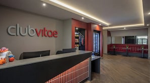 A reception area with a counter, chairs, a red seating area, and a wall with the text 'clubvitoe'.