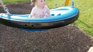 Un niño en un columpio con asiento azul, en un parque infantil con suelo de mantillo.