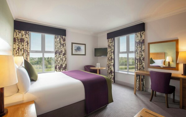 A hotel room with a bed, a desk, a chair, a TV, and large windows with curtains.