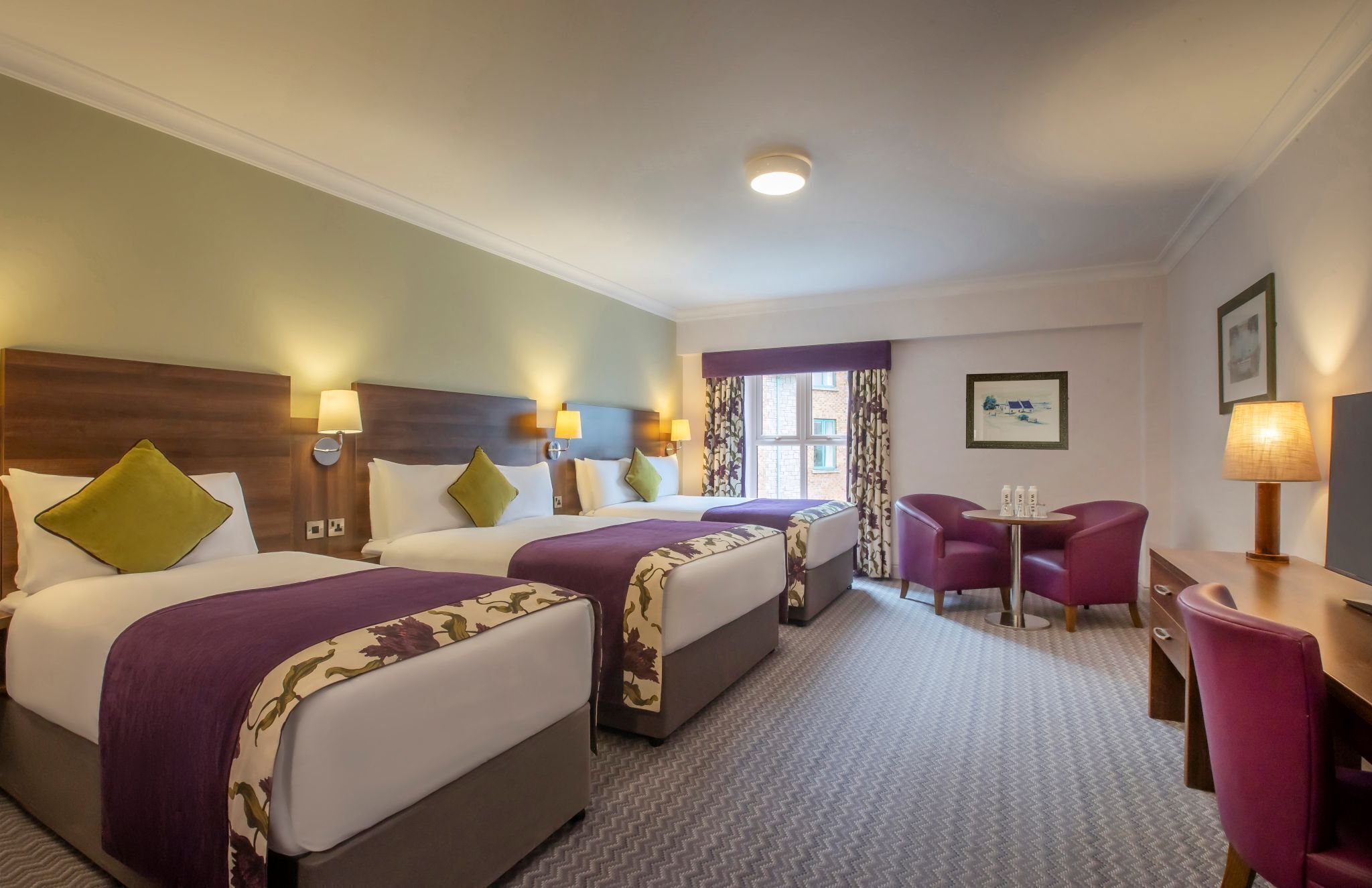A hotel room with two beds, a desk, a chair, and a window with curtains.
