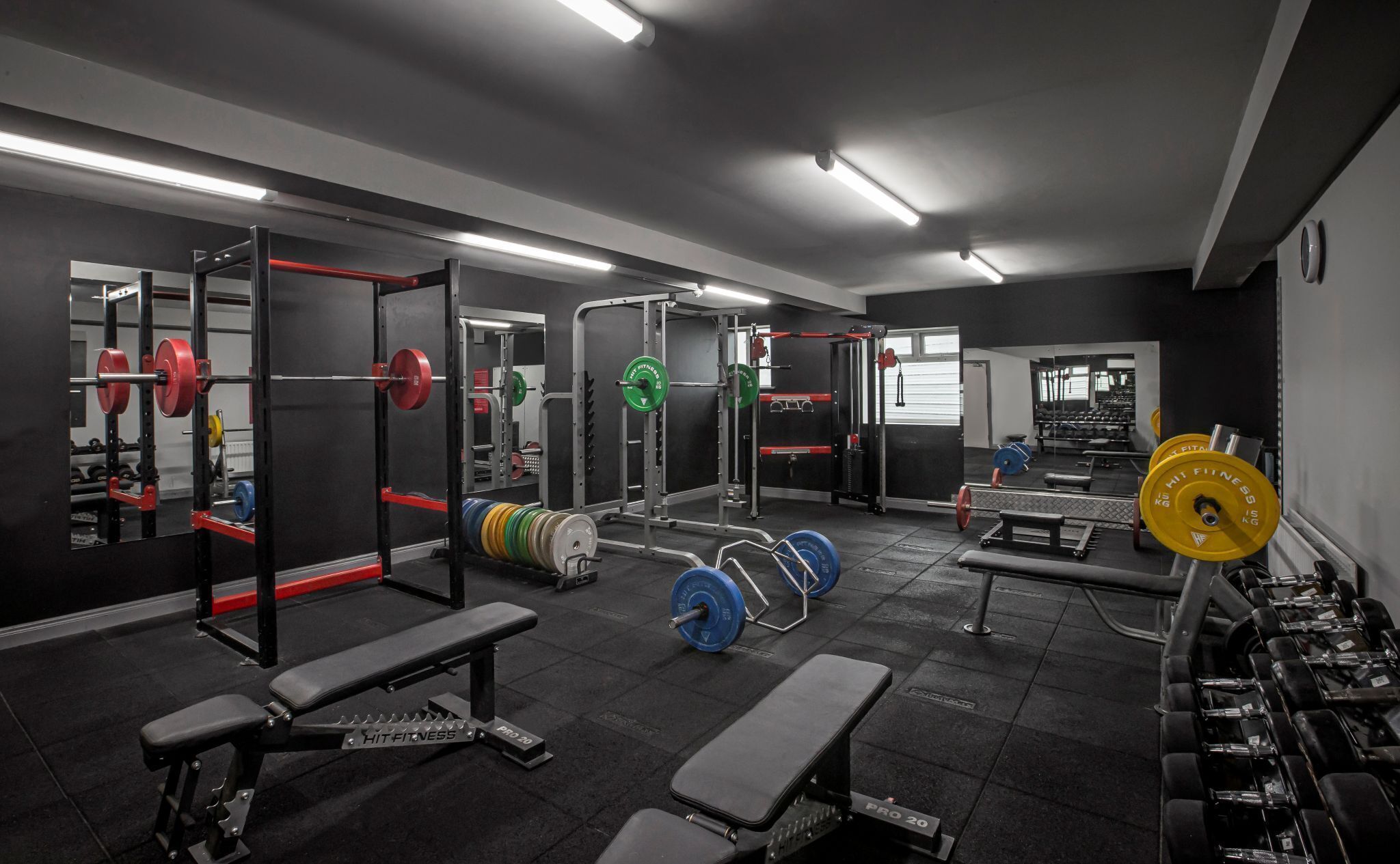 A gym with weightlifting equipment, benches, and a mirrored wall.