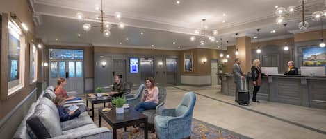 Un vestíbulo de hotel con zonas de estar, un mostrador de recepción y un bar.