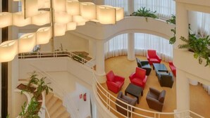 A multi-level hotel lobby with a central staircase, red and black seating areas, and hanging lamps. - Hotel Ceuta Puerta de África (Ceuta)