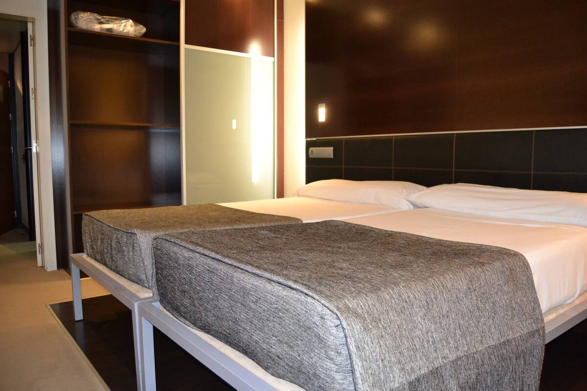Habitación de hotel con dos camas individuales, un armario y un espejo.