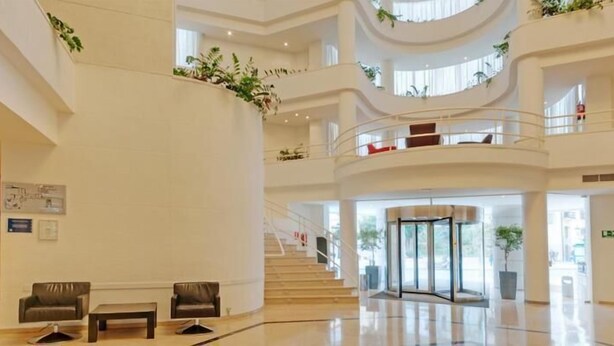 A multi-level hotel lobby with a central staircase, seating areas, and a revolving door. - Hotel Ceuta Puerta de África (Ceuta)