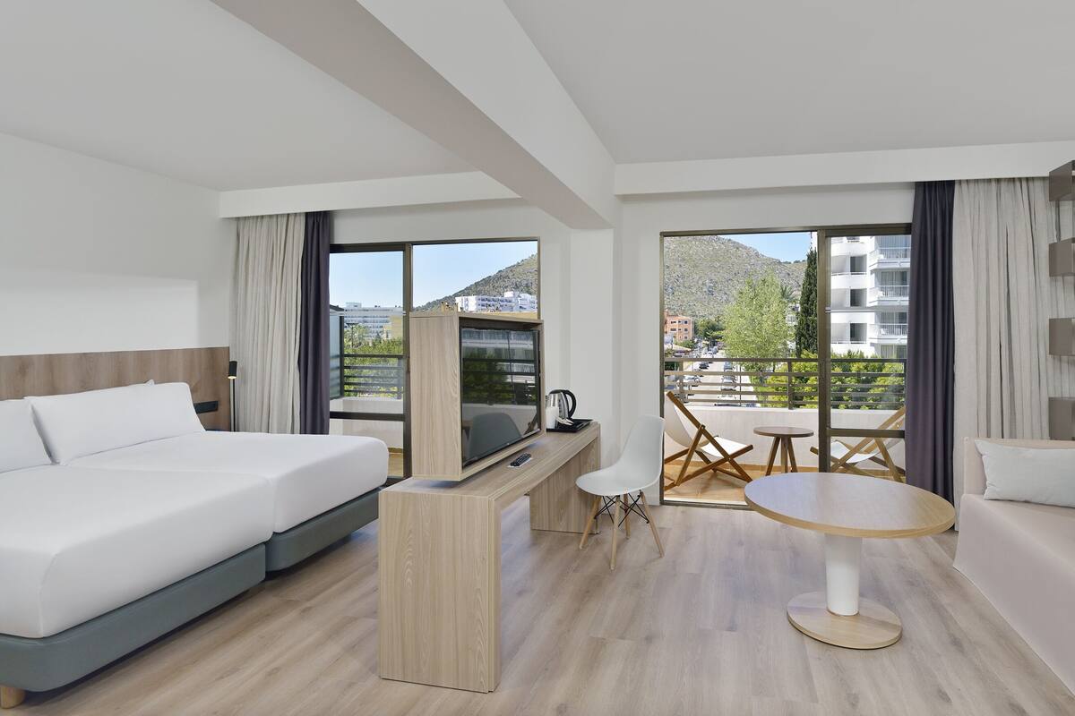 Une chambre d’hôtel moderne équipée d’un lit, d’un bureau, d’une chaise et d’un balcon avec une table et des chaises.