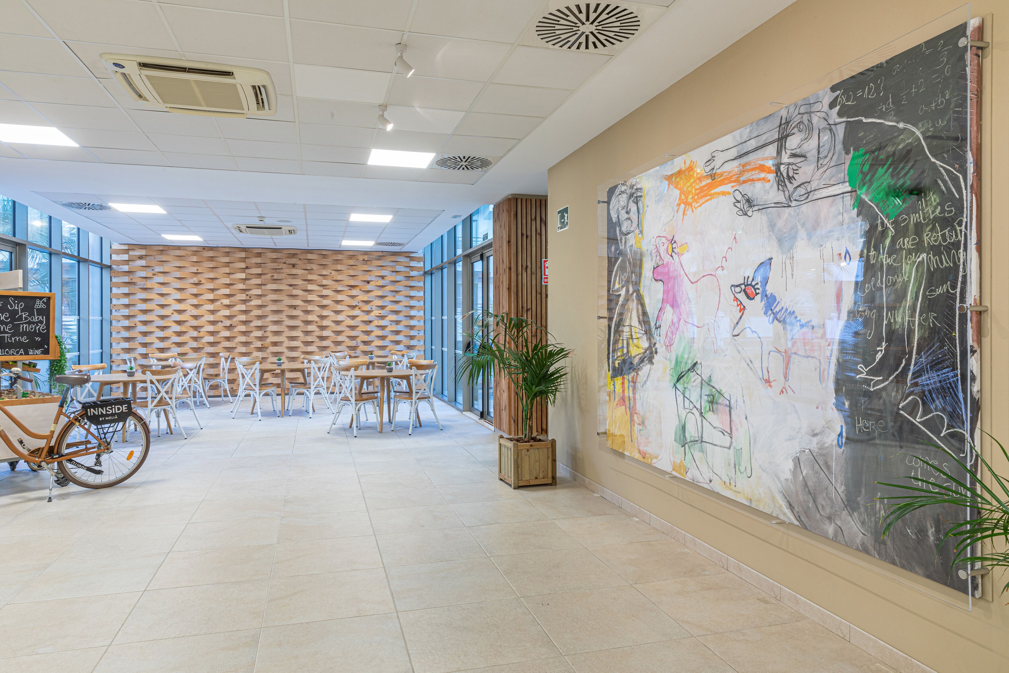 A modern interior with a large abstract mural, a wooden wall pattern, and a seating area with tables and chairs.