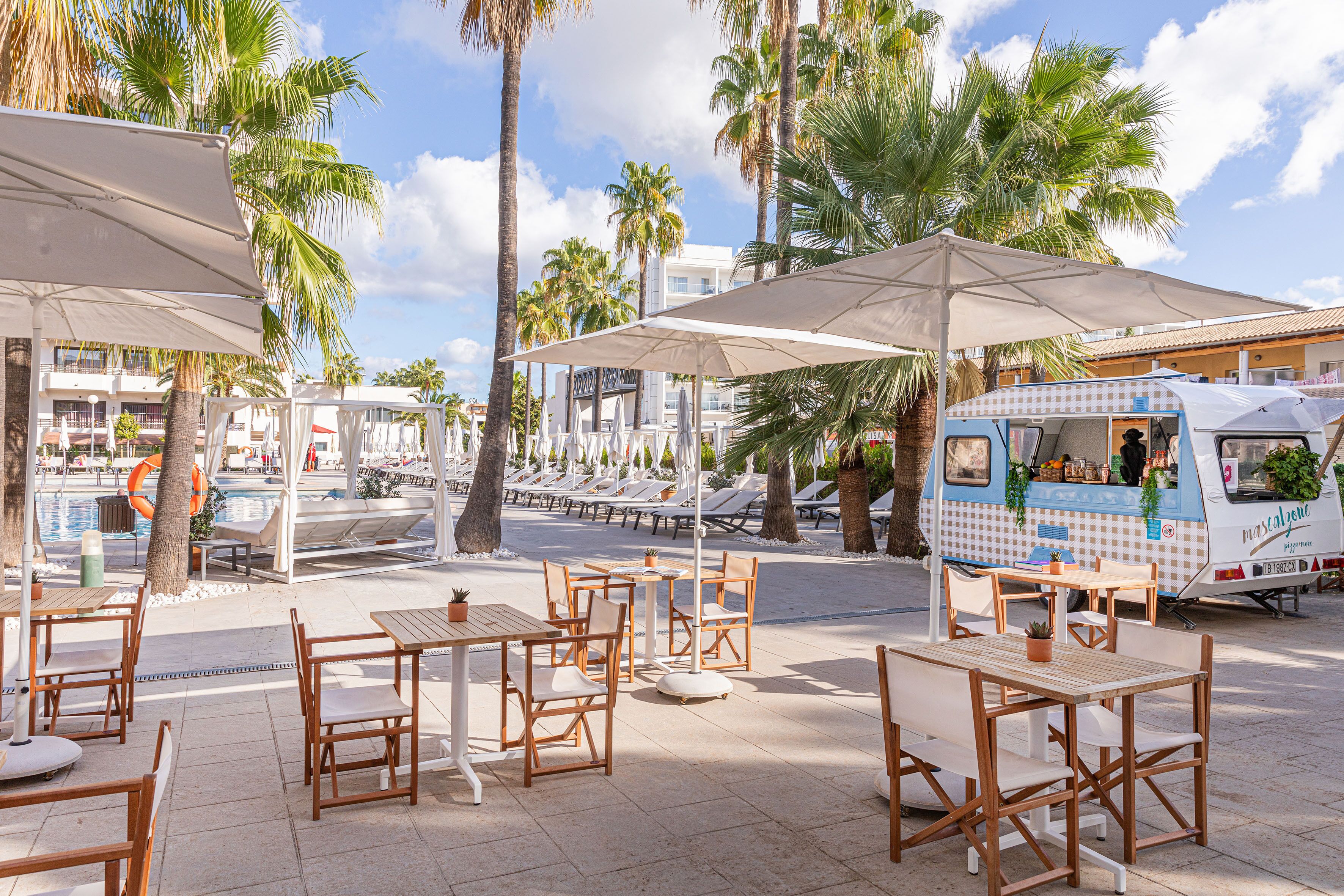 An outdoor dining area with wooden tables and chairs, umbrellas, and a food truck.