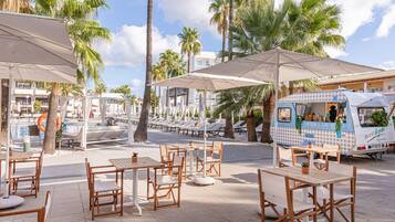 An outdoor dining area with wooden tables and chairs, umbrellas, and a food truck.