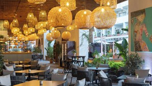 Un vaste espace extérieur aménagé avec des meubles en osier et des lampes suspendues en osier.