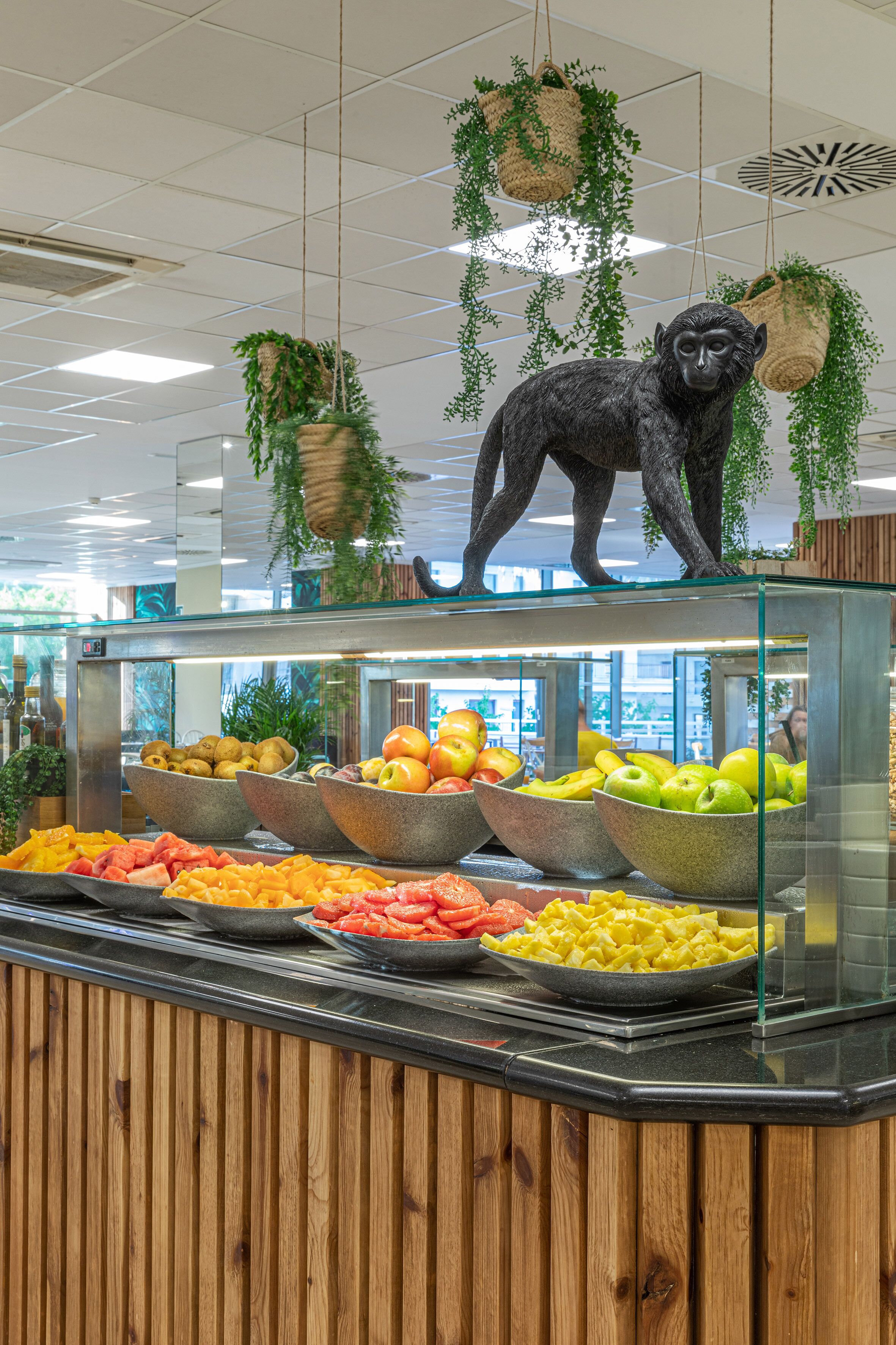 Un espace buffet où diverses sortes de fruits et de légumes sont présentés dans des bols, avec une statue de singe au sommet et des plantes suspendues.