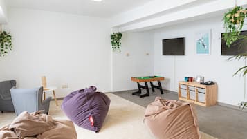 Un salon moderne avec une table de billard, des fauteuils poire, un fauteuil bleu et une petite table sur laquelle est posé un arbre à chat.