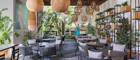 An outdoor café with wicker furniture, hanging wicker lights, and potted plants.