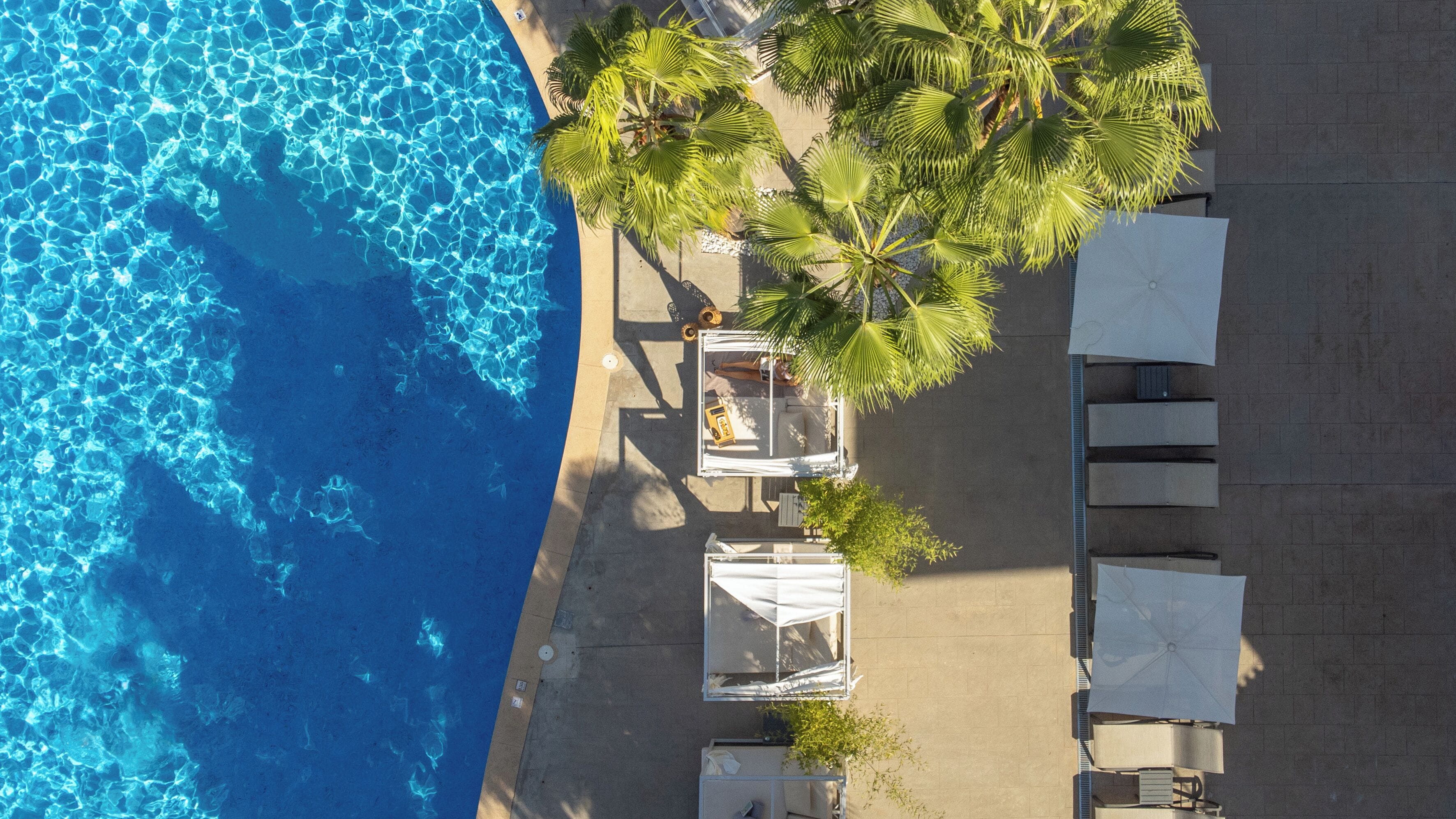An aerial view of a beachside hotel with a pool, palm trees, and outdoor seating.