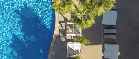 An aerial view of a beachside hotel with a pool, palm trees, and outdoor seating.