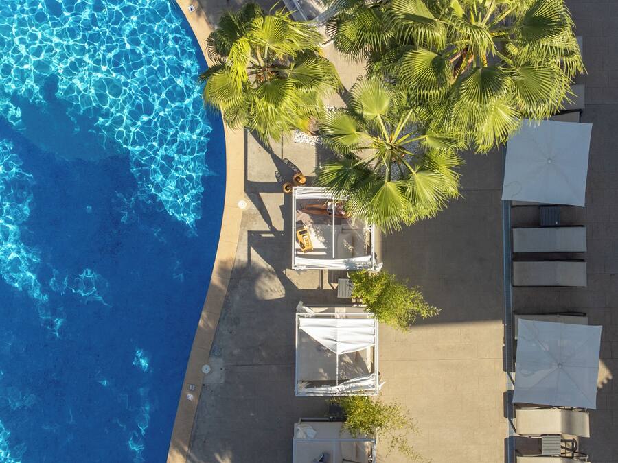An aerial view of a beachside hotel with a pool, palm trees, and outdoor seating.