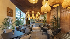Un espace de restauration intérieur aménagé avec des meubles en osier, des luminaires suspendus en osier et offrant une vue sur l’extérieur.