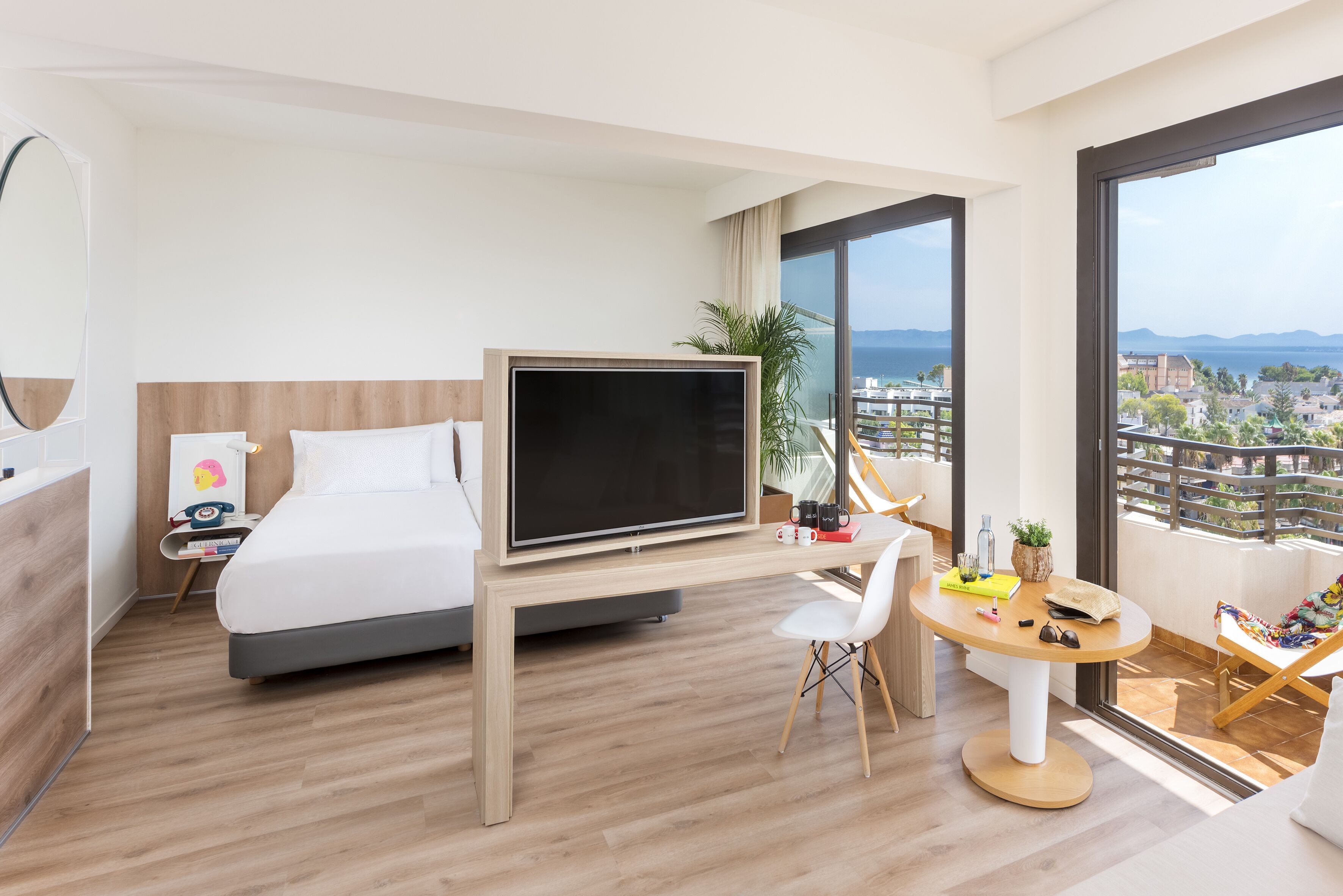 Una habitación de hotel moderna con cama, televisor, escritorio y balcón con vistas a la ciudad.