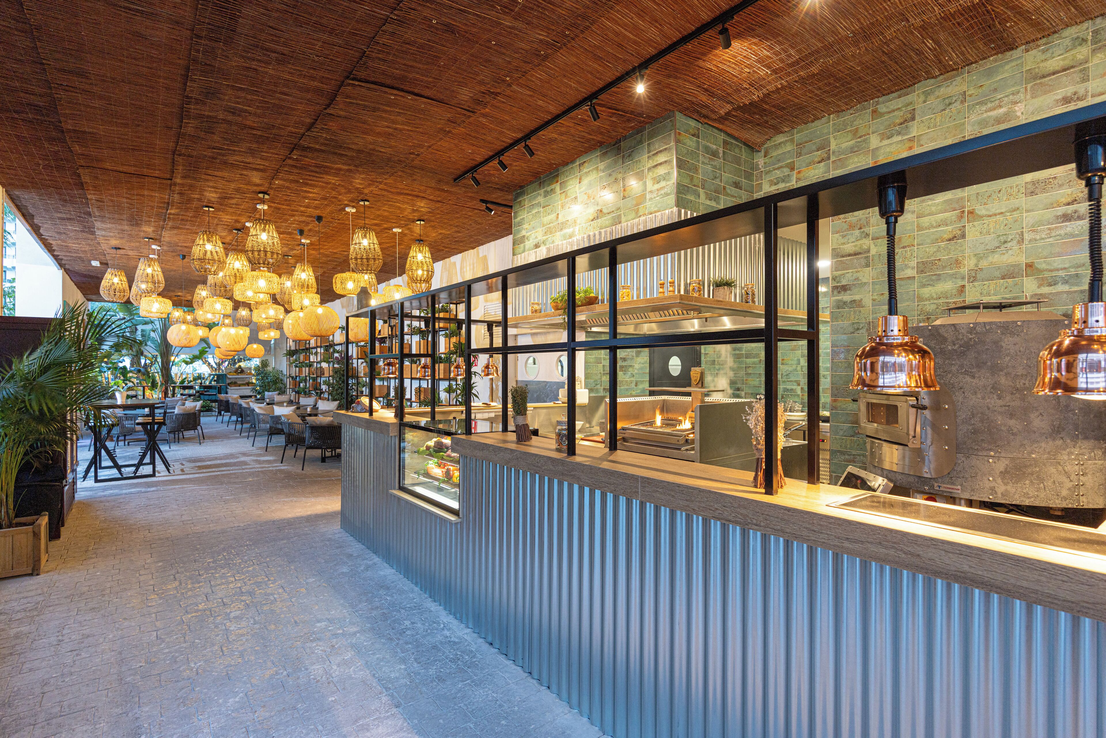 Un restaurante con techo de madera, luces colgantes y una barra con vista a la cocina.