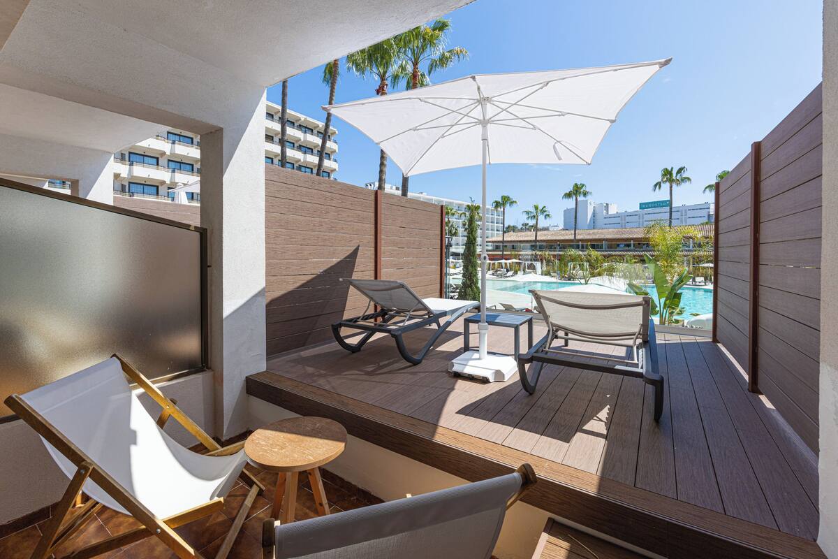 Un balcon avec vue sur la piscine, une terrasse en bois et des chaises longues.