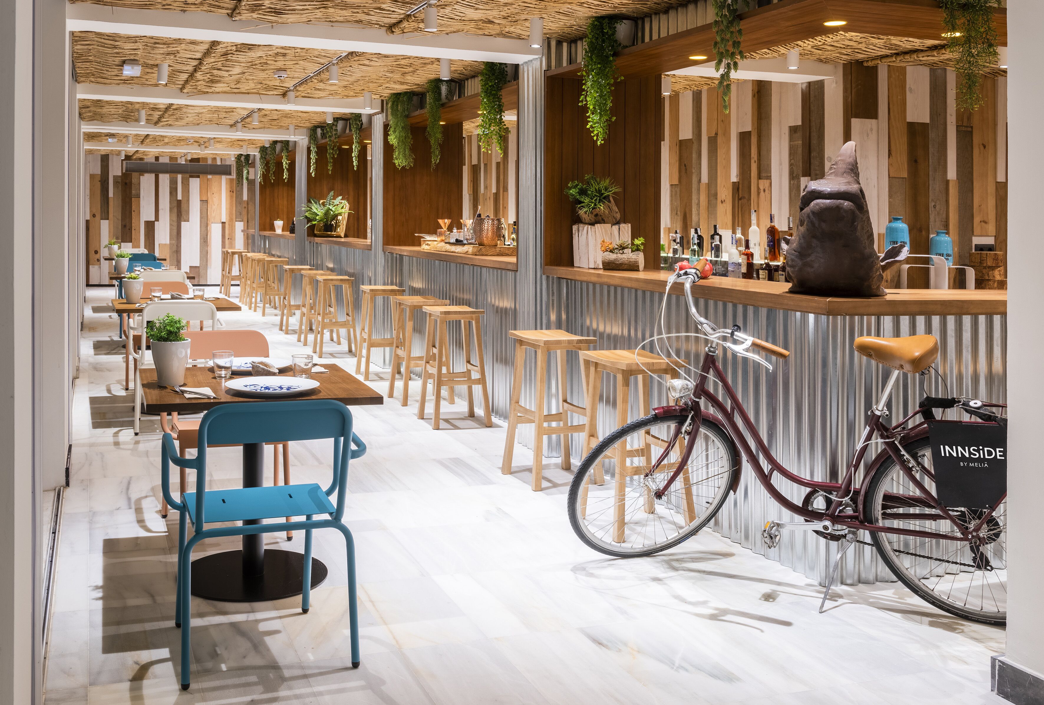 A modern bar area with wooden stools, a bicycle, and a counter with plants and bottles.