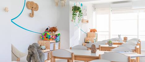 A classroom with wooden tables and chairs, educational materials, and decorative elements like a giraffe sculpture and hanging plants.