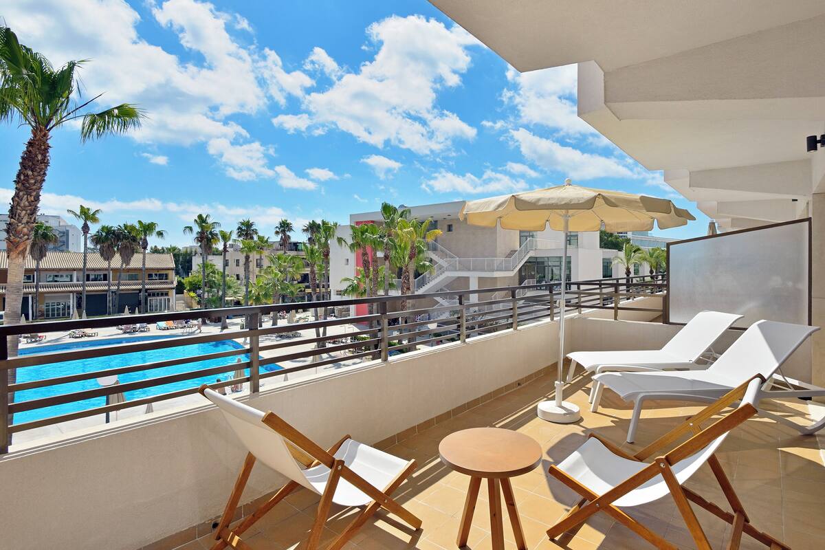 A balcony with white lounge chairs, a small round table, and a pool view.