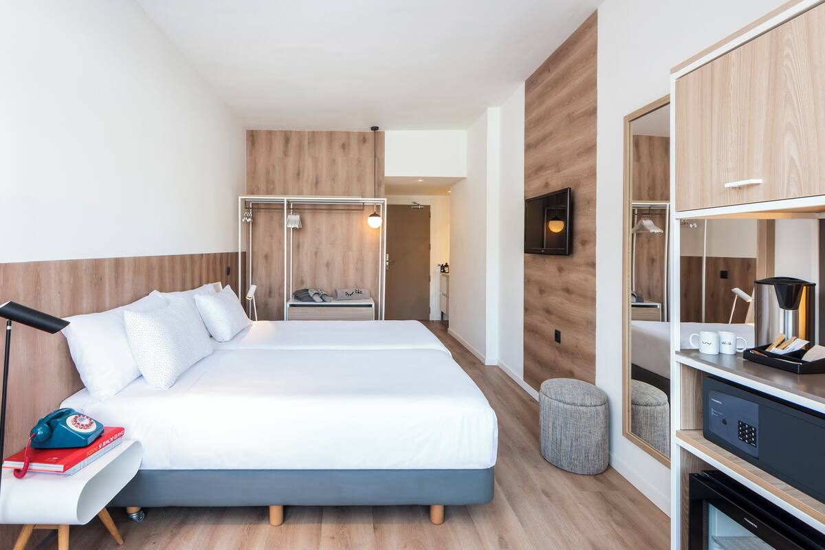 A modern hotel room with a large bed, bedside table, and a wardrobe.