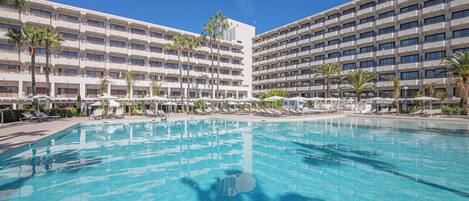 Un grand hôtel à plusieurs étages, doté d’une piscine et bordé de palmiers.