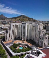 A high-rise hotel with multiple floors, a rooftop pool, and a view of the city and a mountain in the background.