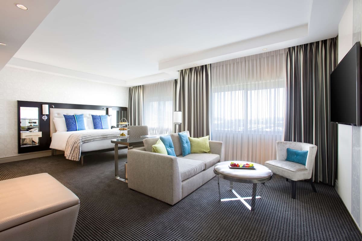 A hotel room with a bed, a sofa, a small table, a chair, and a TV.