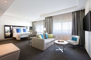 A hotel room with a bed, a sofa, a small table, a chair, and a TV.