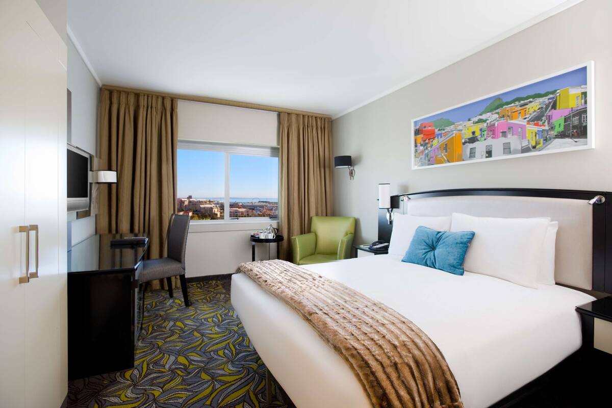 A hotel room with a large bed, a desk, a chair, a TV, and a painting on the wall.
