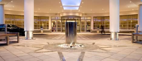A spacious lobby with a central water feature, large windows, and a modern architectural design.