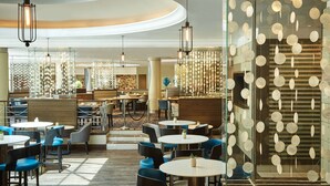 A modern restaurant with round tables and blue chairs, featuring hanging light fixtures and a patterned wall. - Southern Sun Cape Town Waterfront (Cape Town)