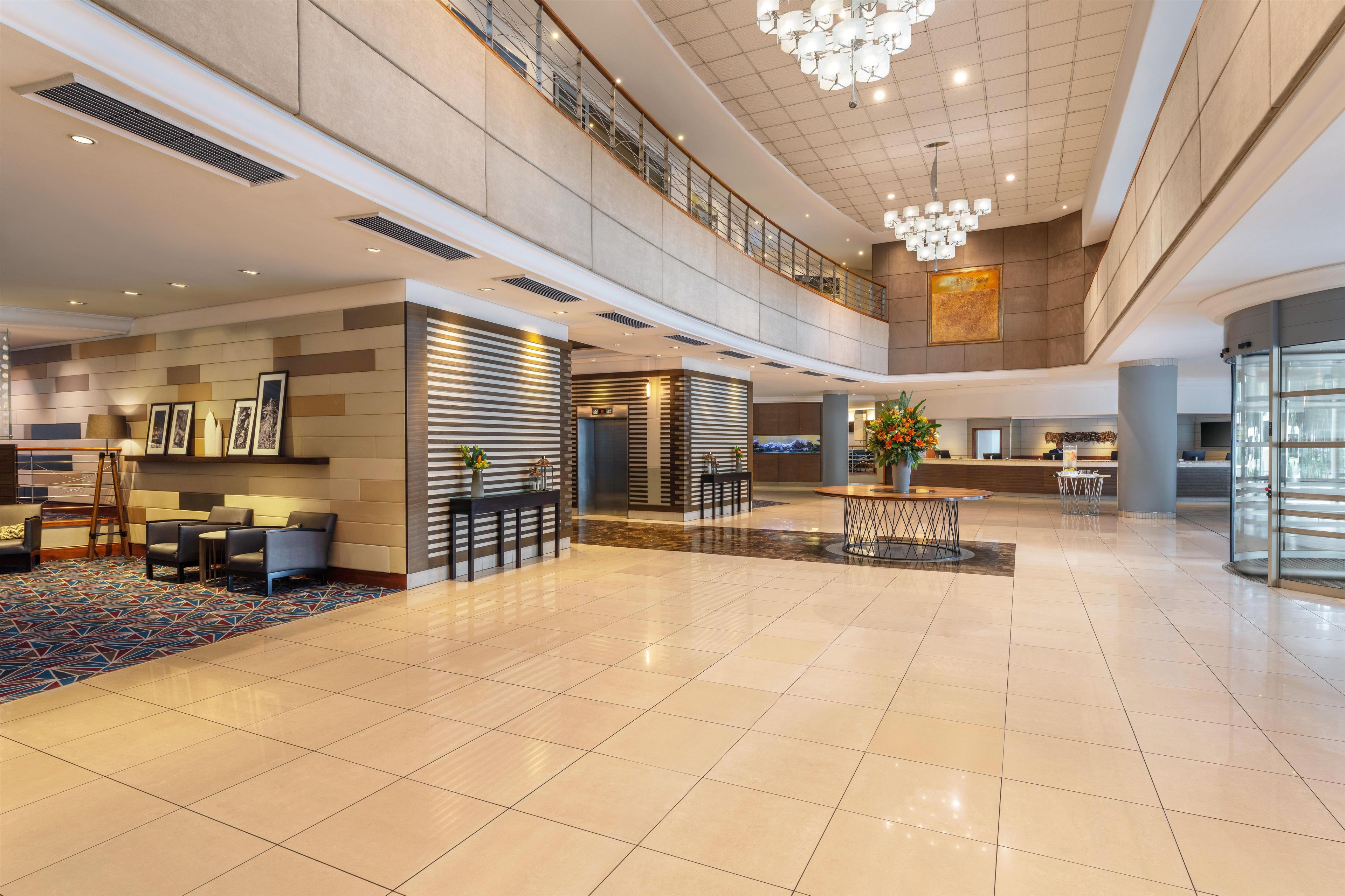 A spacious lobby with a high ceiling, a reception desk, seating area, and a staircase leading to an upper level.