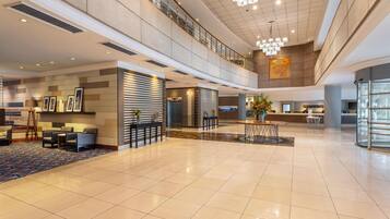 A spacious lobby with a high ceiling, a reception desk, seating area, and a staircase leading to an upper level.